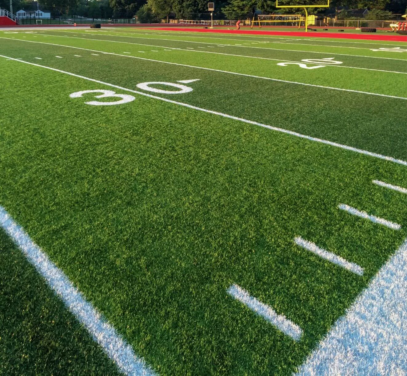 A football field in Glendale, AZ, boasts bright green artificial turf installed by expert artificial grass installers. Marked with white lines and numbers, including the 30-yard line in focus, it features yellow goalposts and a red running track under a clear sky.